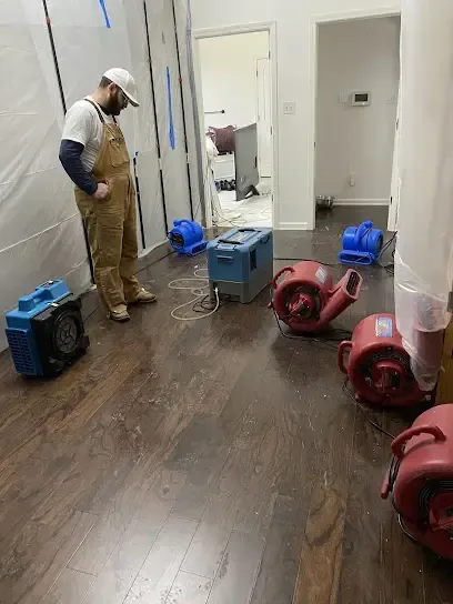 Restoration technician checking air movers and plastic containment during a dry-out