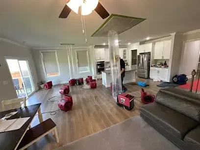 Open-plan living room with red air movers on the floor and a section of ceiling opened for drying
