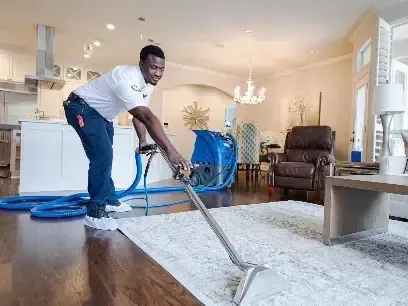 Technician running an extraction wand across a living room rug to pull out standing water