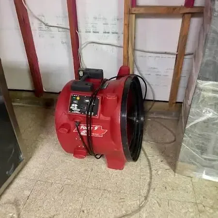Red air mover in a room with an opened wall and hanging plastic sheeting