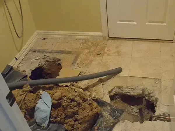 Tile and concrete slab broken open beside a doorway to reach a leaking pipe