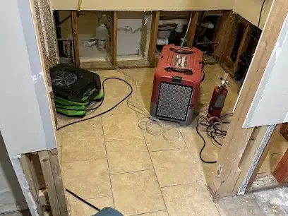 Air movers and a dehumidifier drying a room with opened walls